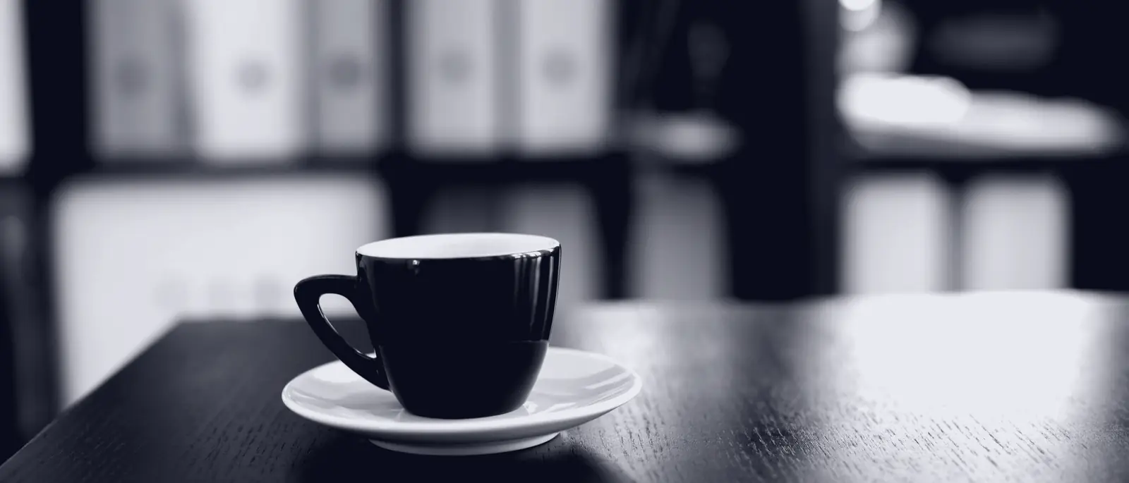 A quiet desk with a coffee cup, duotoned to the FlatHours navy.