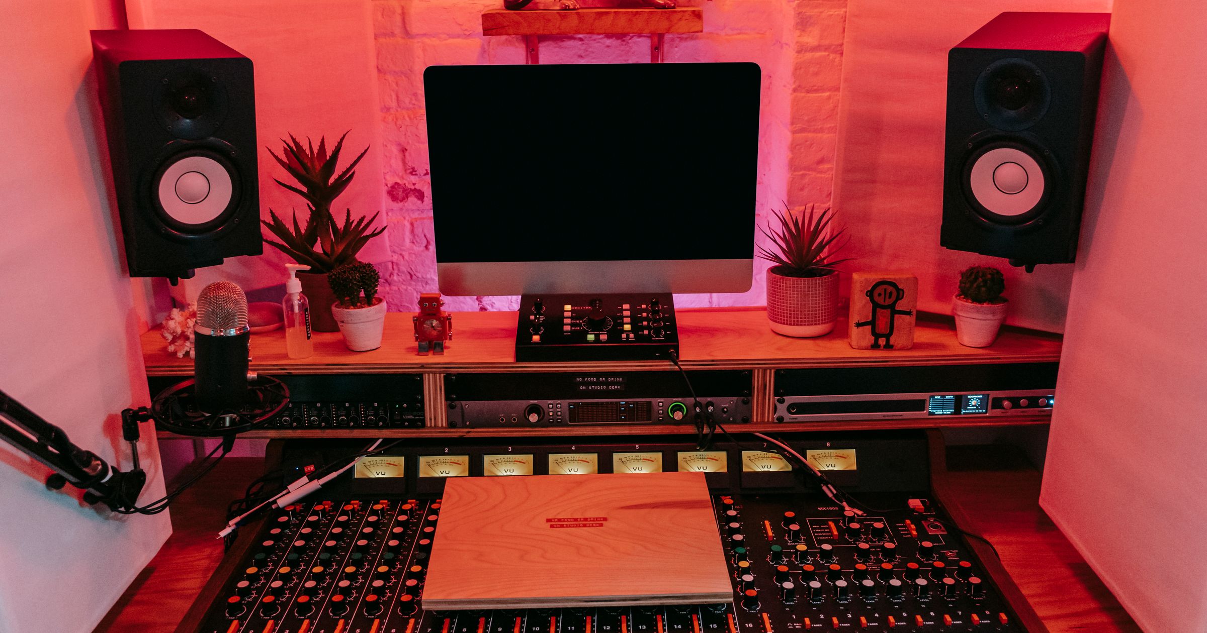 A clean wooden studio desk with a laptop displaying project files, a notebook, and a coffee mug.