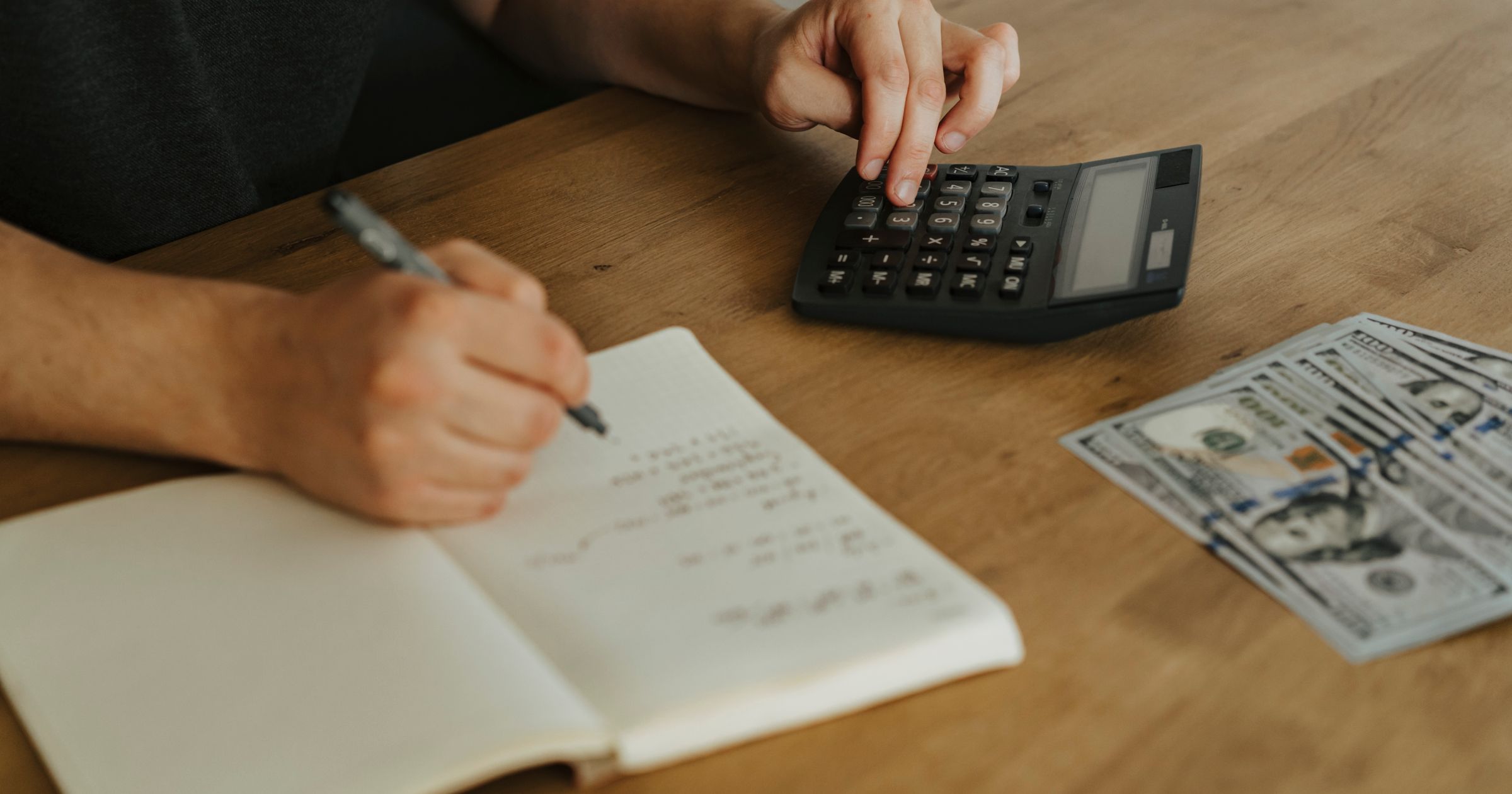 A clean wooden studio desk with a notebook, pen, laptop, and financial ledgers laid out neatly.